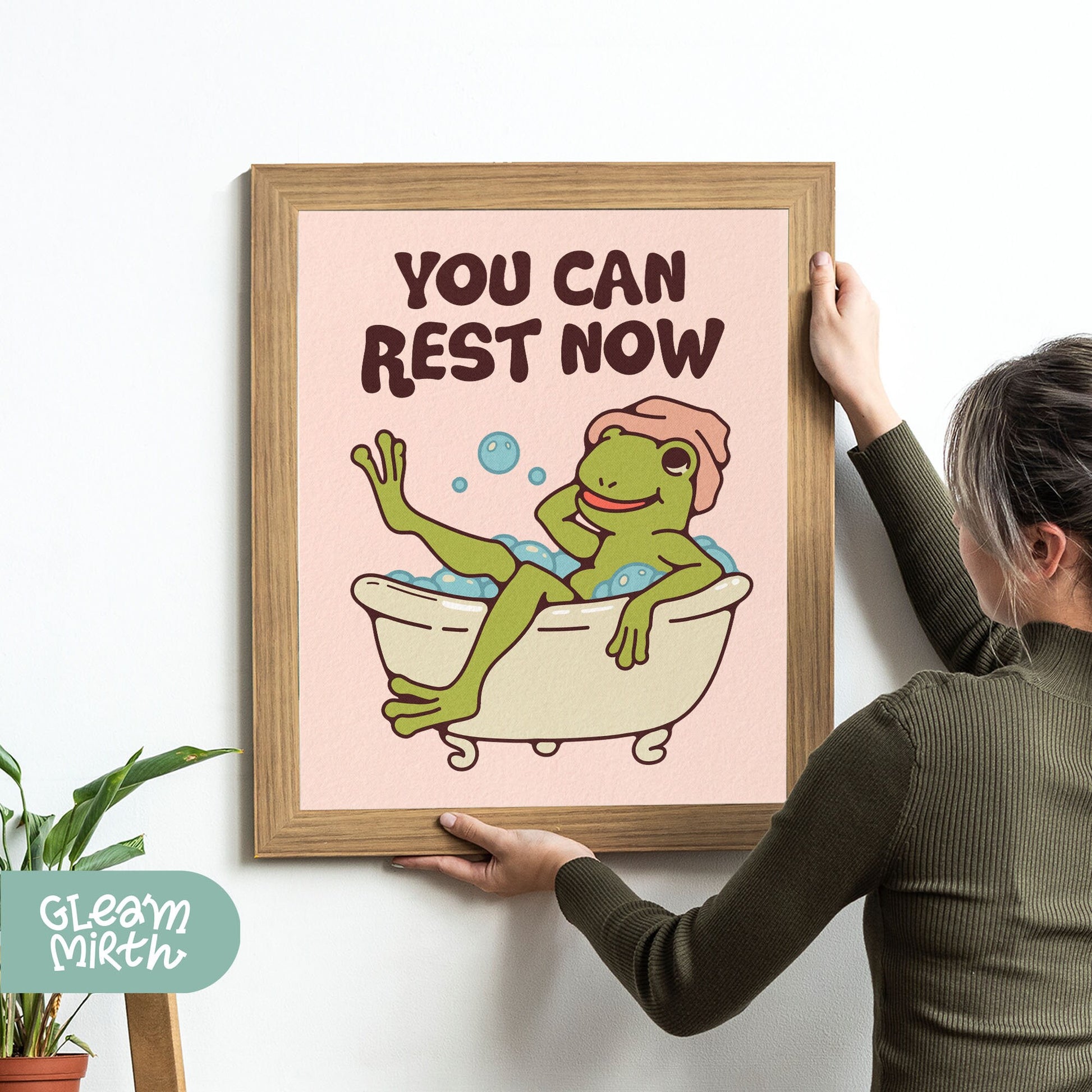 a woman holding up a picture of a frog in a bathtub