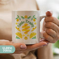 a woman holding a coffee mug with a lemon design on it