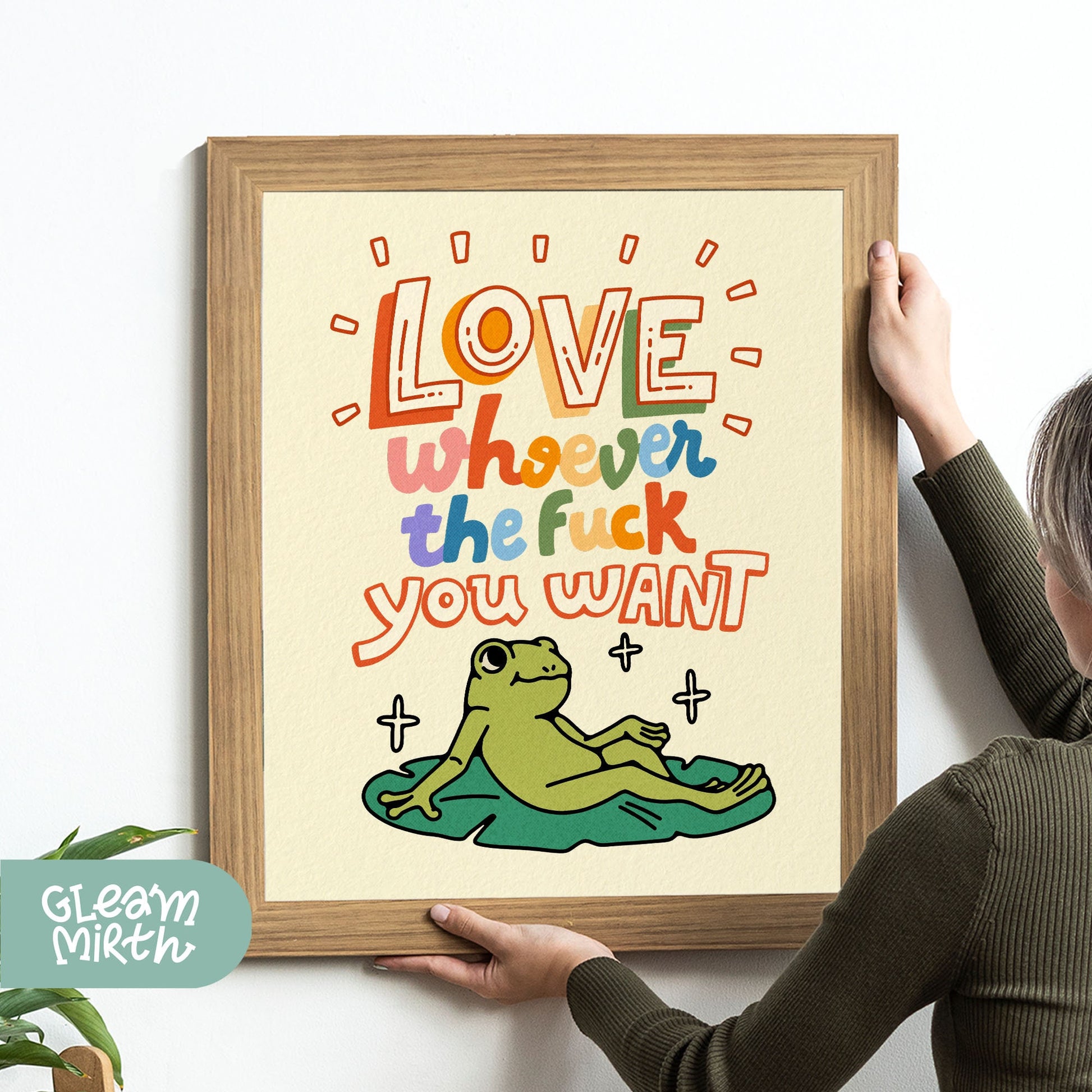 a woman holding up a framed poster with a frog on it