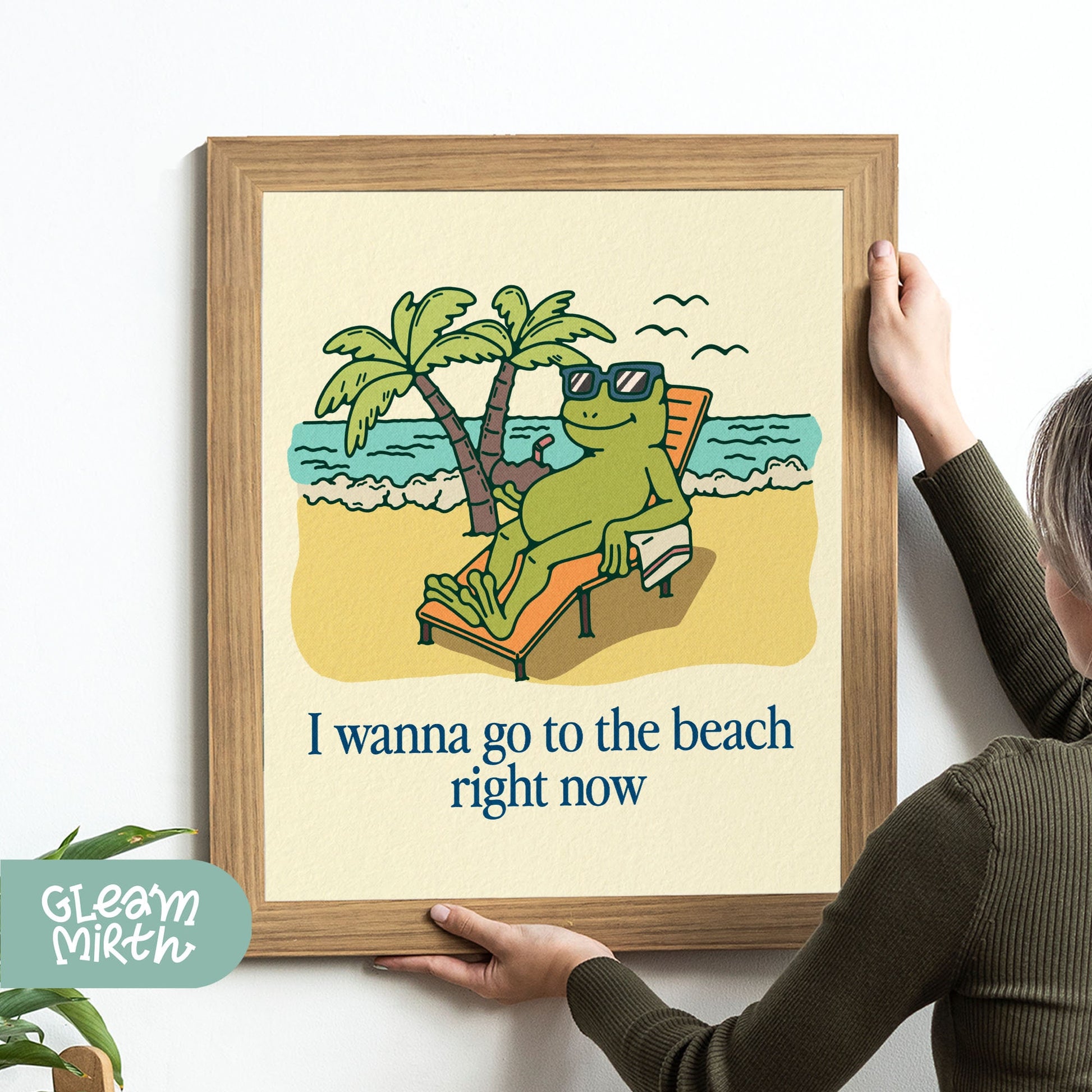 a woman holding up a picture of a frog on the beach